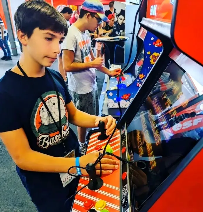 Un jeune joueur découvre une borne Neo Geo lors d’un événement Arcade Pyrénées